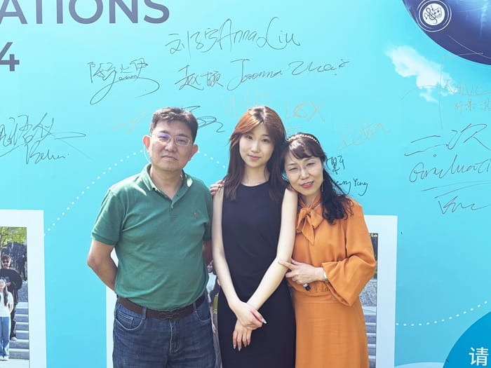 Bella with her parents in front of the graduation backdrop